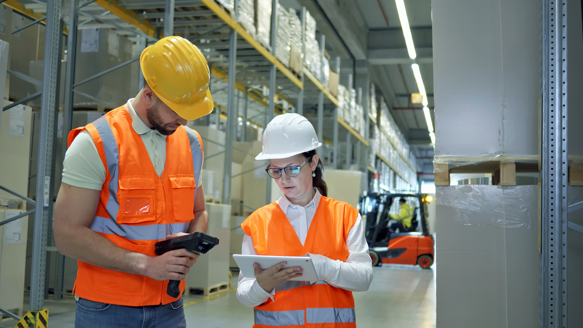 Warehouse workers in safety vests and helmets reviewing logistics data on a tablet